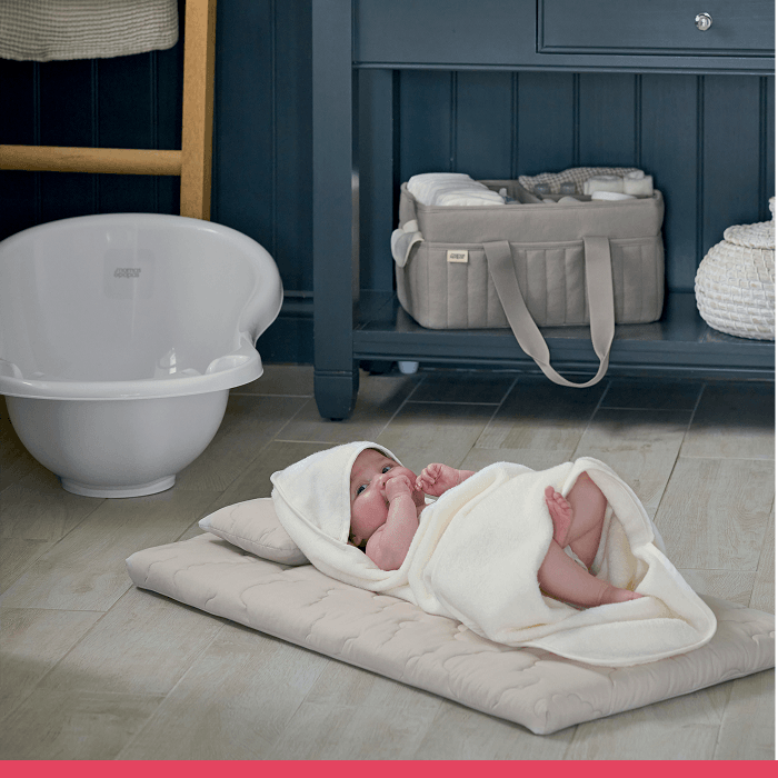 A baby wrapped in a blanket on a changing mat in a nursery.