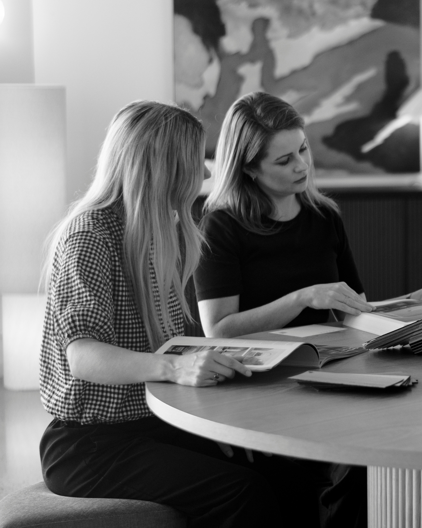 Two women discussing a magazine at a round table in a modern setting.