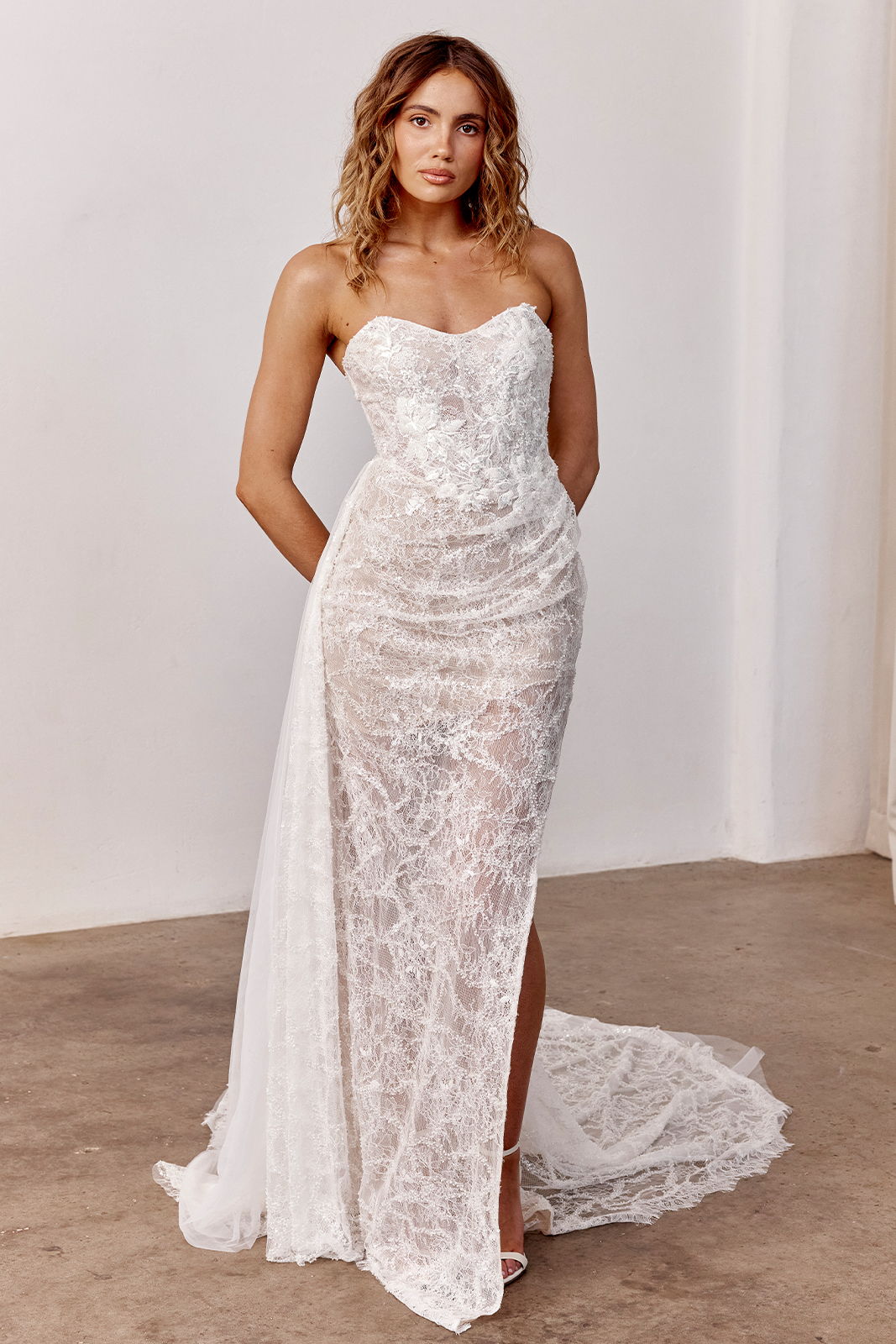 Woman wearing a strapless white lace dress with a thigh-high slit.