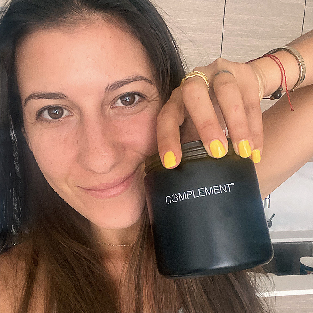 Woman holding Complement Essential vegan multivitamin glass jar. 