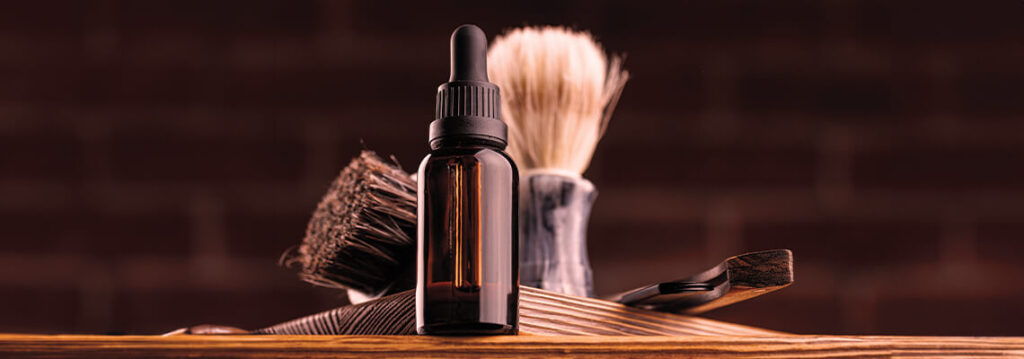 A shaving brush and a bottle on a wooden surface against a brick background.
