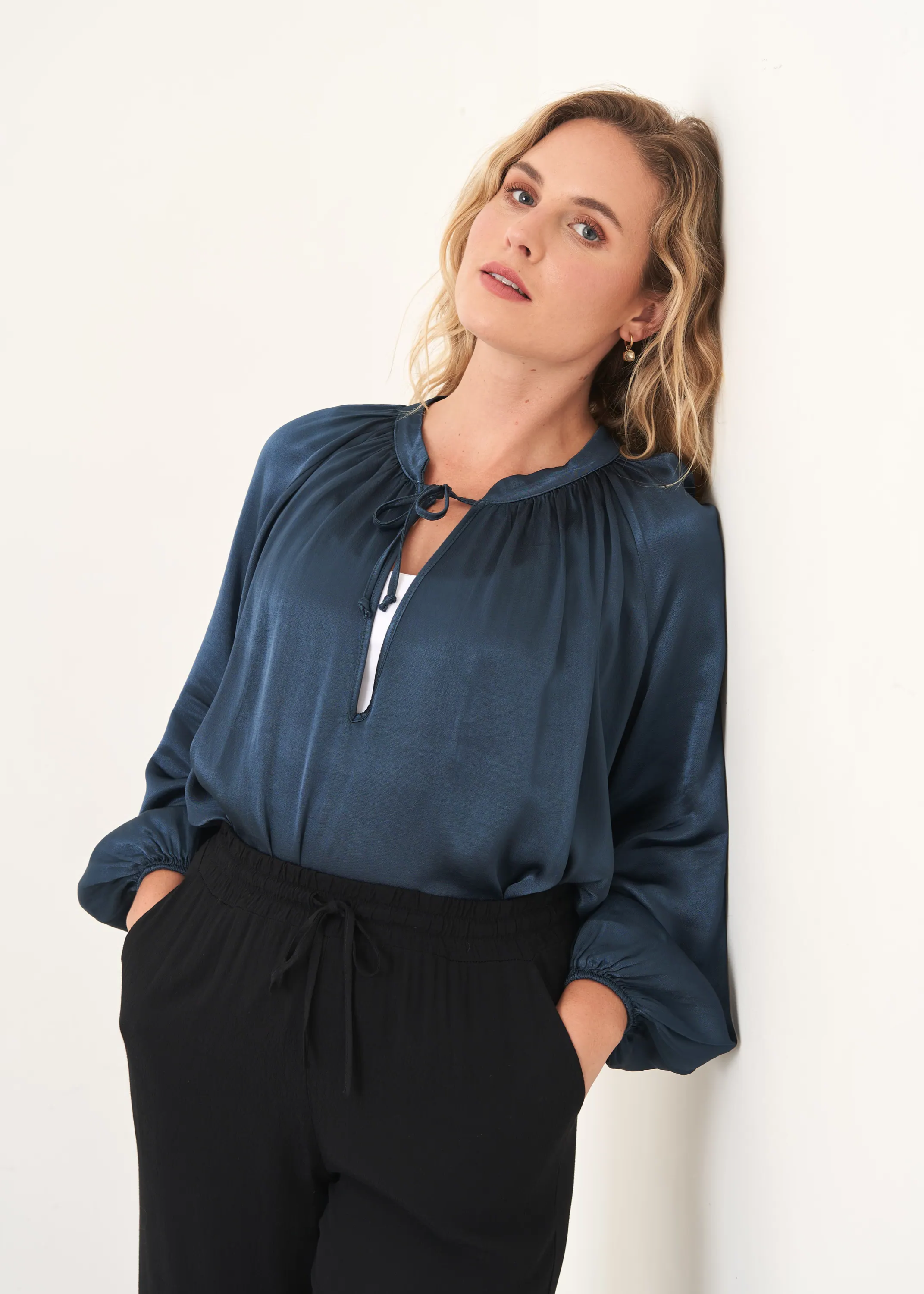 A model wearing a dark teal, satin oversized long sleeved blouse