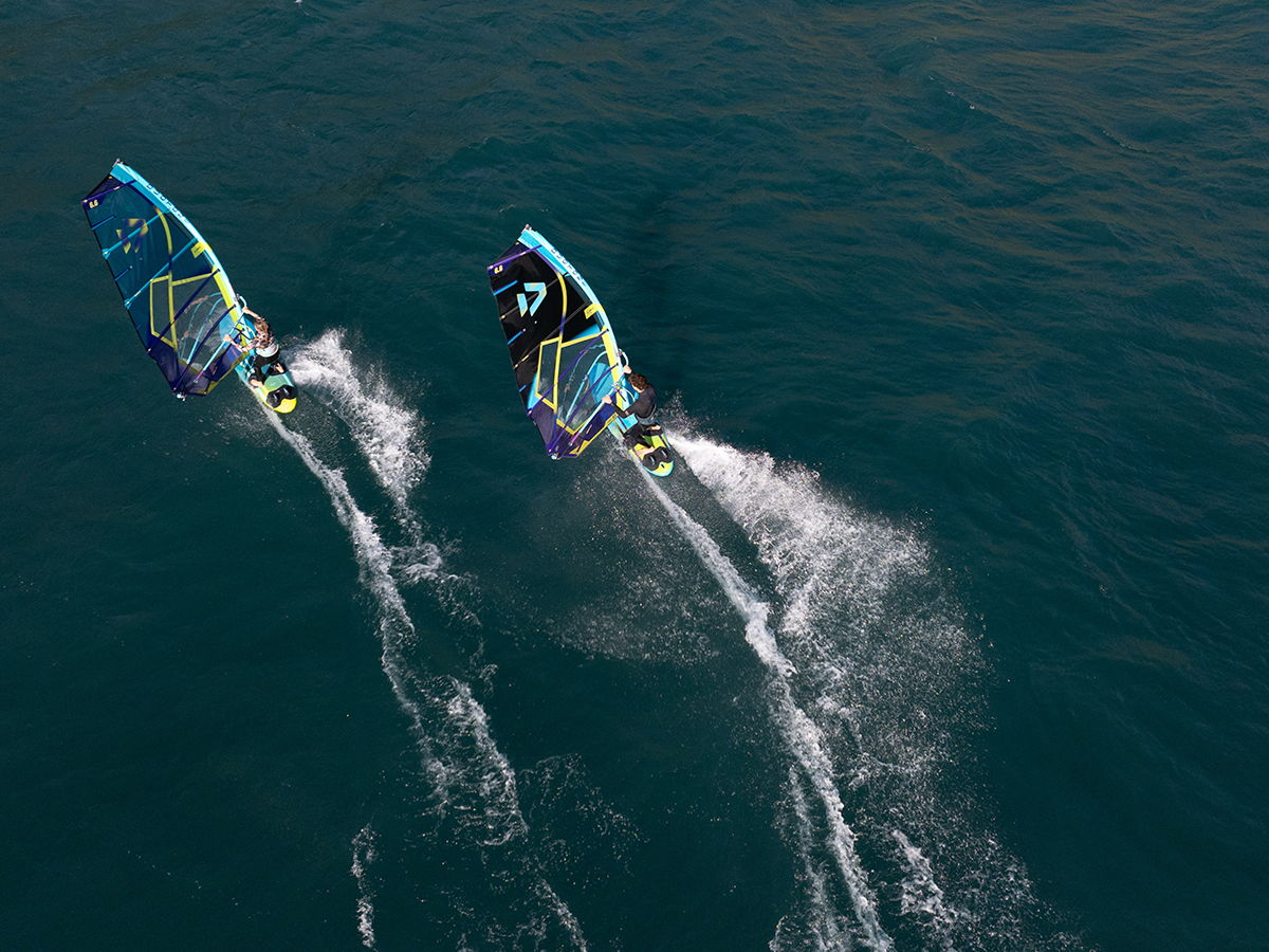 Two windsurfers gliding over the water, leaving trails behind.