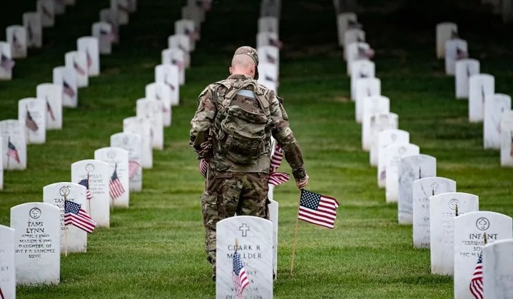 Soldier placing flags at gravestones in a cemetery.