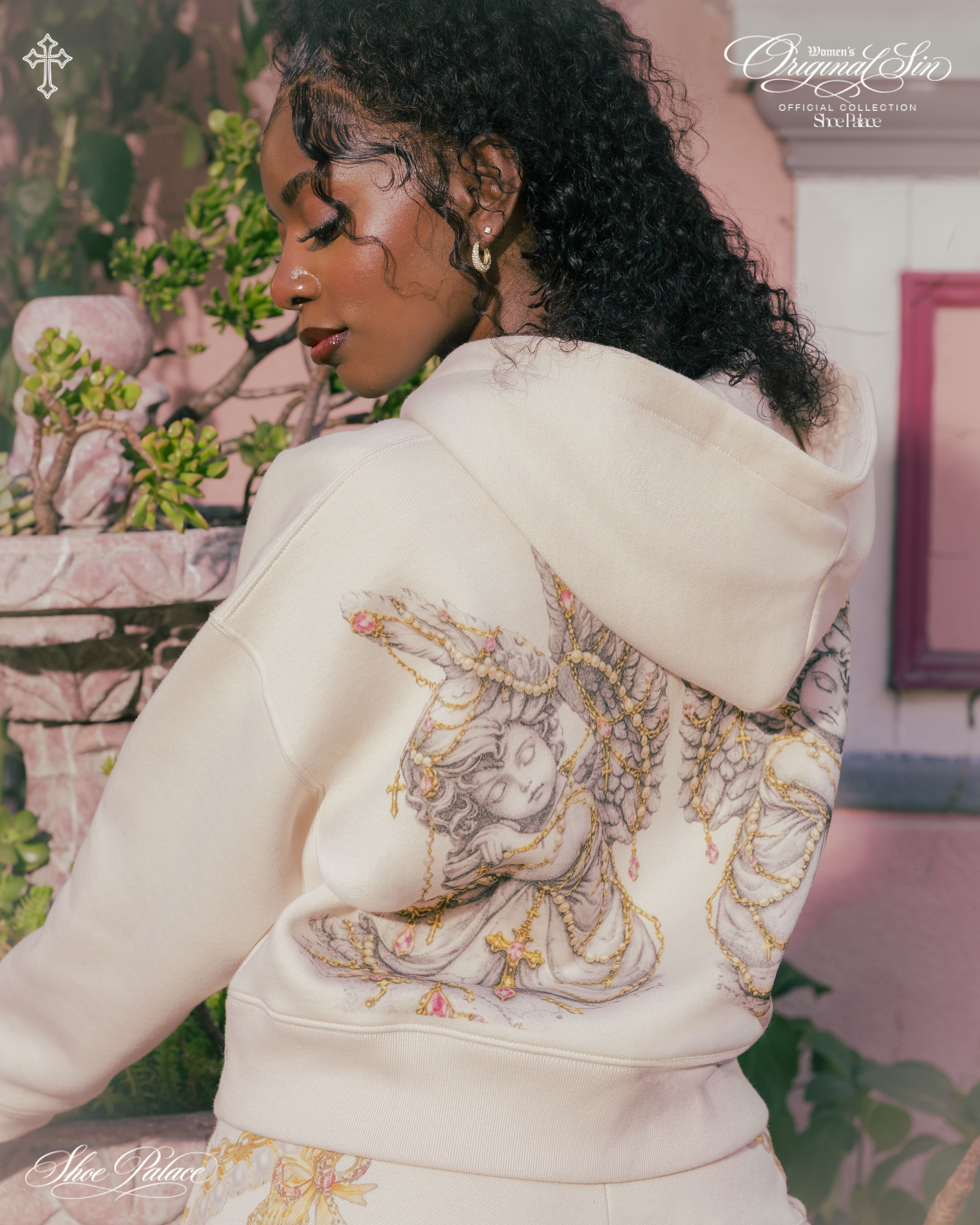 Woman wearing a cream hoodie with intricate back design, posing outdoors.