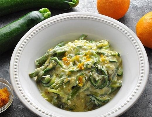 Creamy zucchini pasta garnished with orange zest, served in a white bowl.