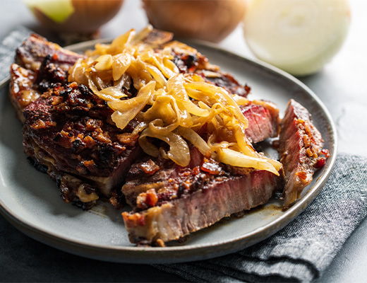 Cooked meat with caramelized onions on a plate, garnished with vegetables.