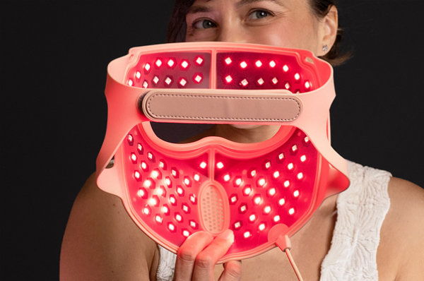 Woman holding a red light therapy mask with a smiling expression.