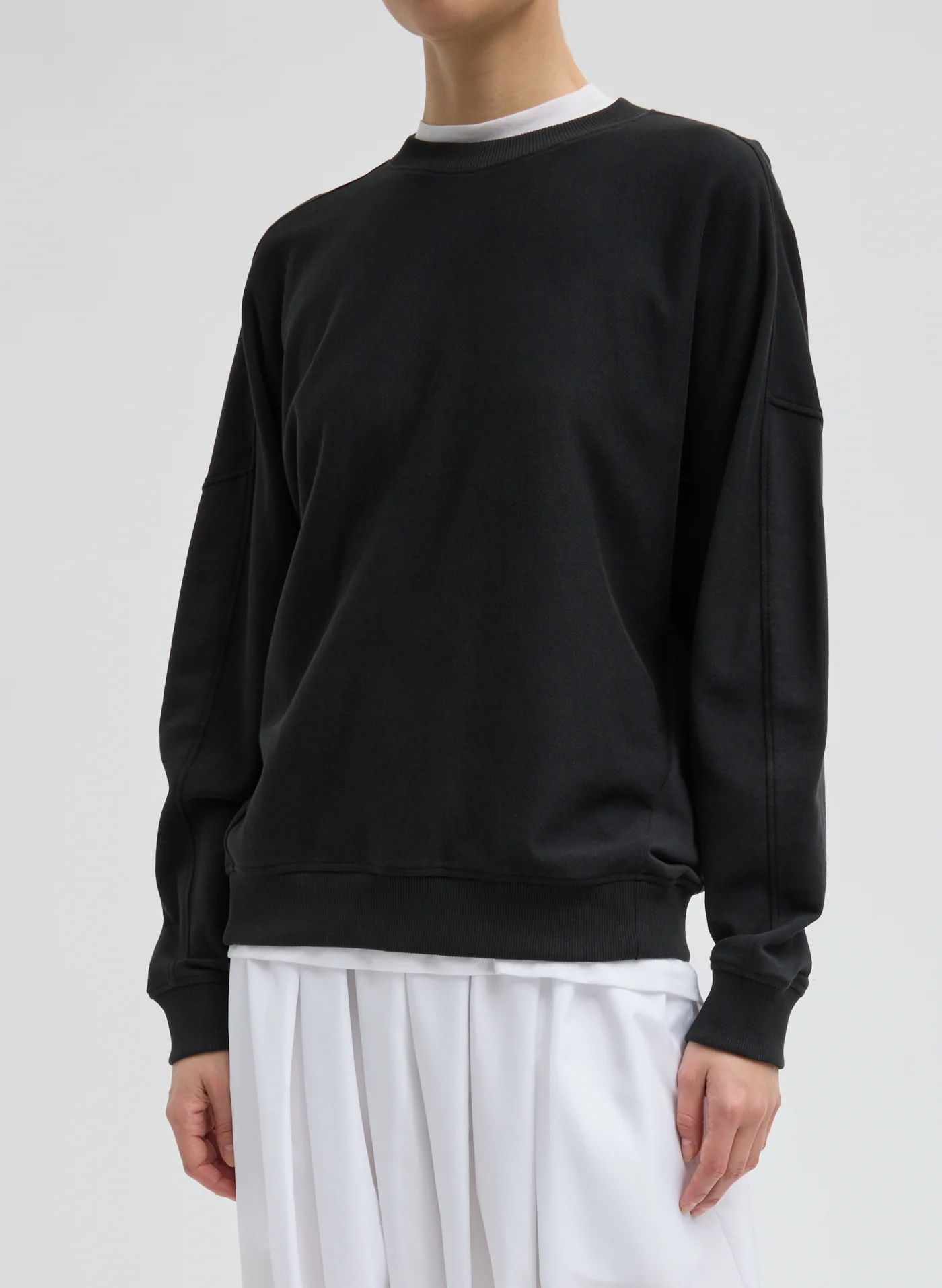 Person wearing a black sweatshirt and white pants against a neutral background.