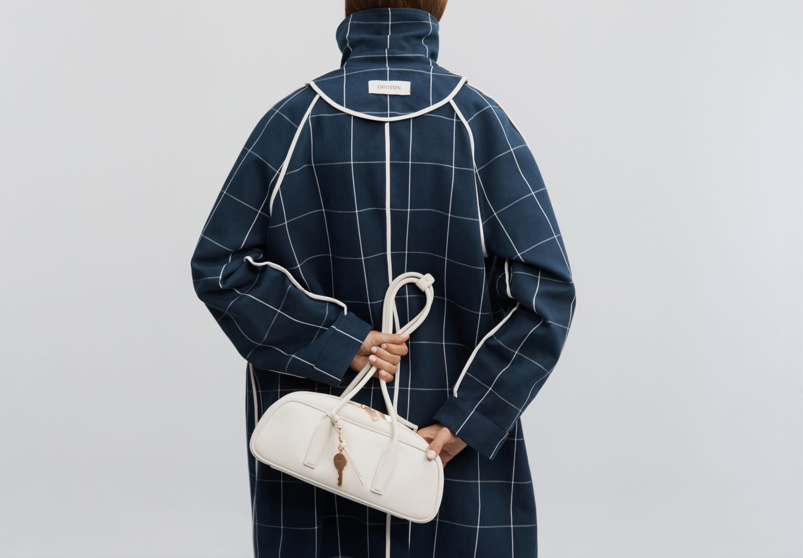 Person wearing a plaid coat holding a white handbag from behind.
