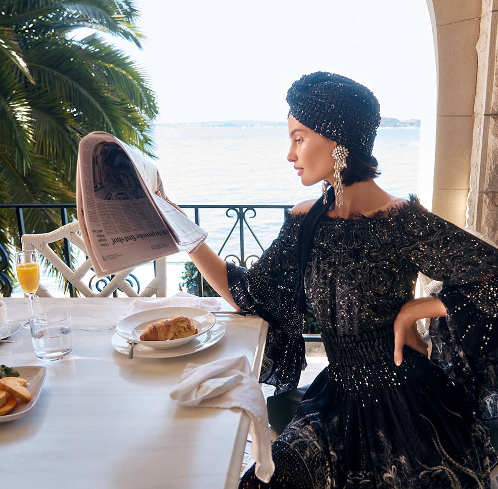 Model reading newspaper over breakfast in CAMILLA black and silver embellished off shoulder blouse and skirt with sequin turban.