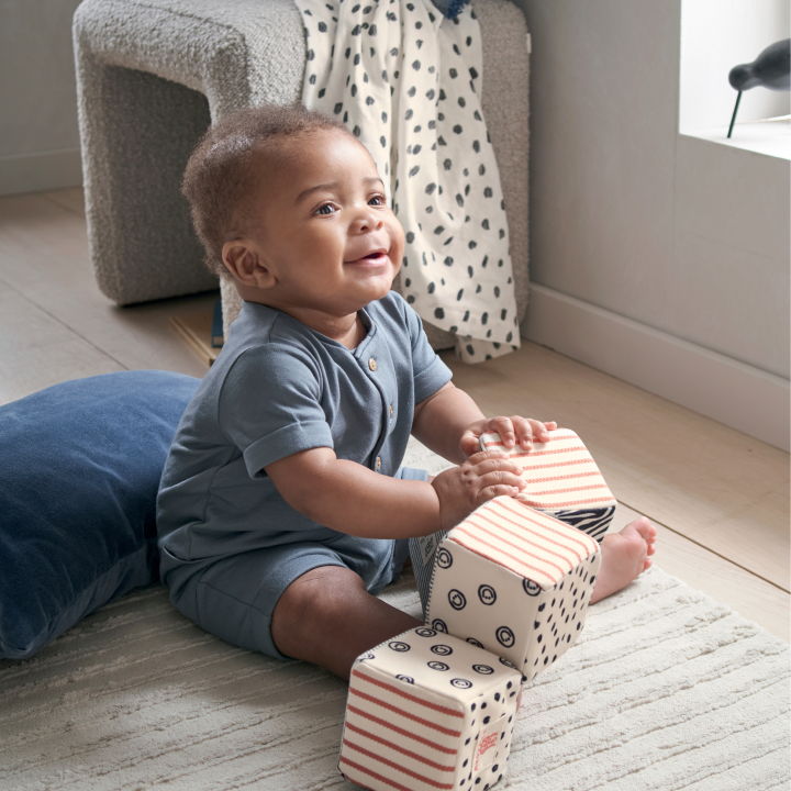 A happy baby sitting on a rug with colorful blocks.