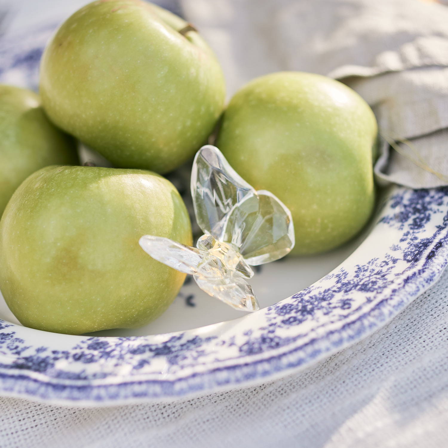 A butterfly fairy light on a plate with green apples.