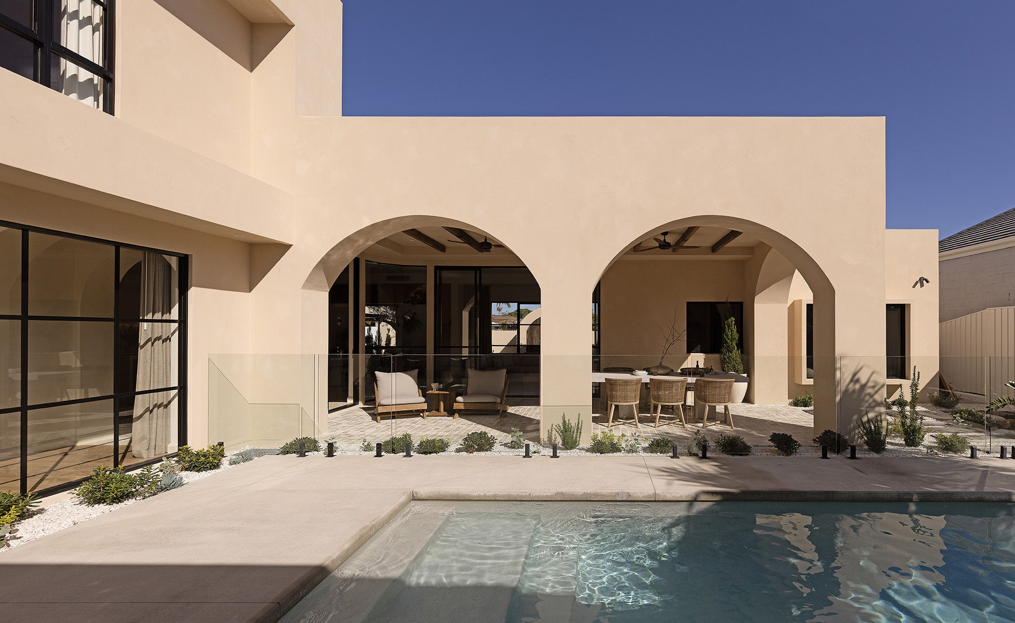 Modern home exterior with pool and arched doorways under a clear blue sky.