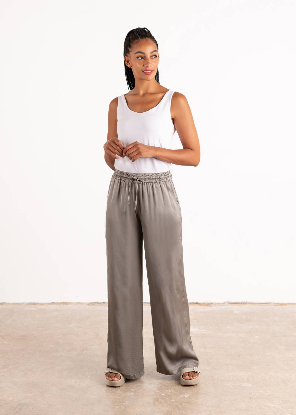 A model wearing a white sleeveless vest with silvery satin wide leg trousers