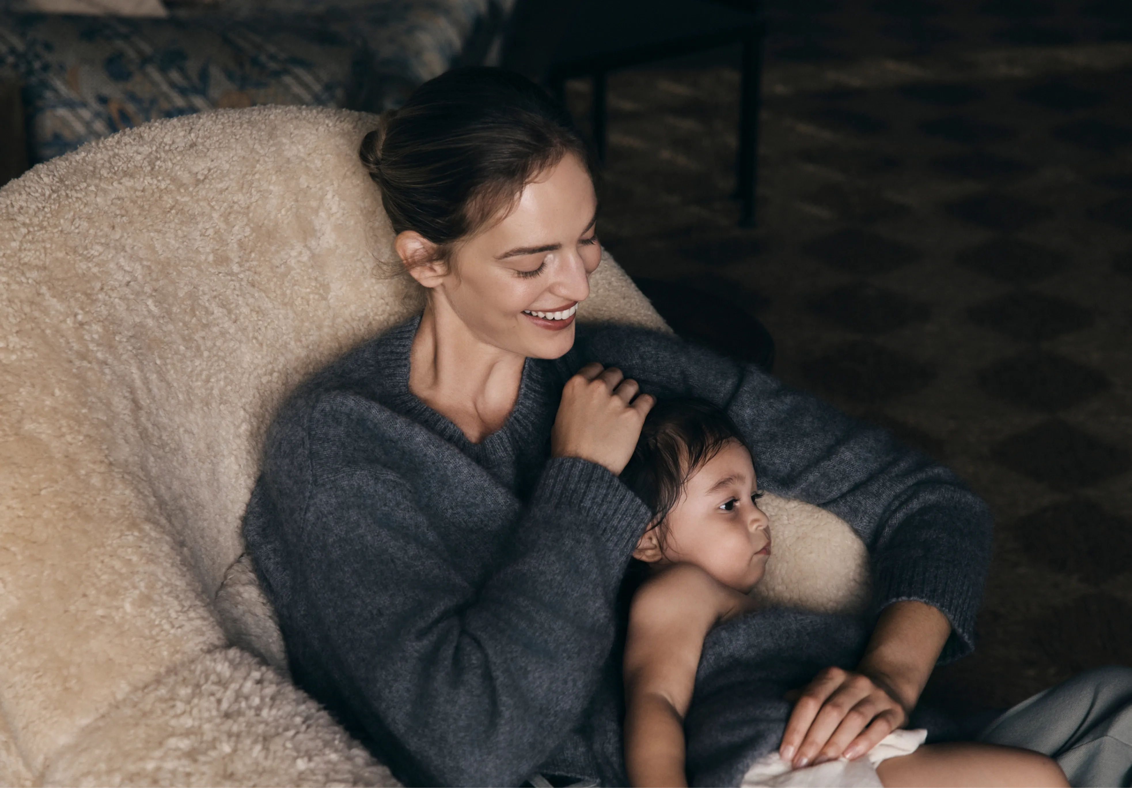 Woman sitting in a chair with a child, both looking content.