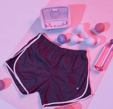 Fotografia de shorts de ginastica com halteres, um perfume e um rádio ao fundo 