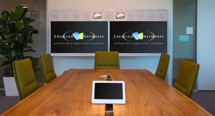 Conference room with a wooden table, chairs, and two screens.
