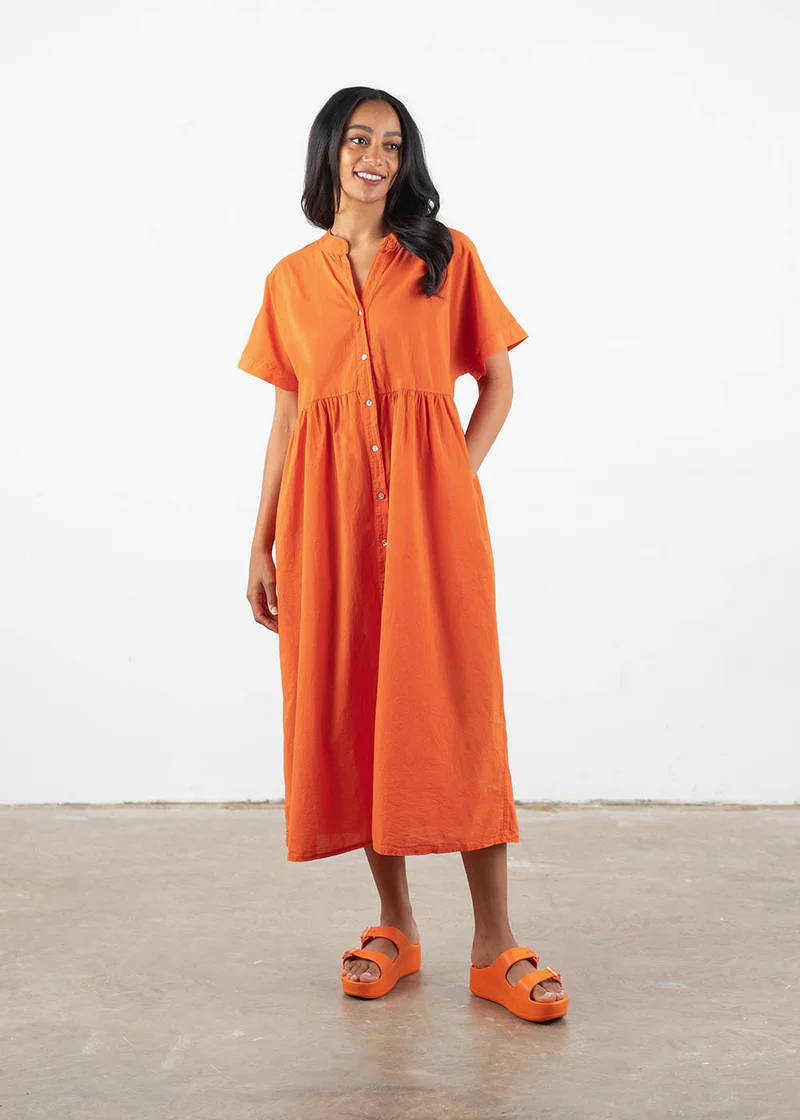 A model wearing a bright orange oversized dress with short sleeves and mother of pearl buttons down the front with matching orangy chunky platform slides