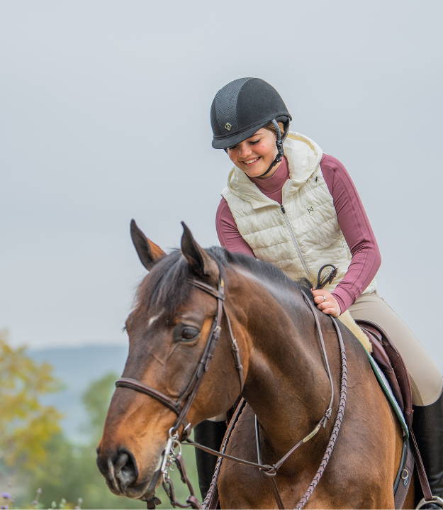 Girl in pink sunshirt and white vest petting her horse in bridle and martingale