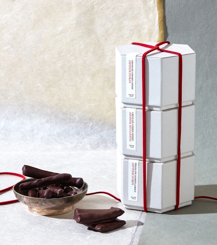 Stack of white boxes tied with red ribbon beside a bowl of chocolate treats.