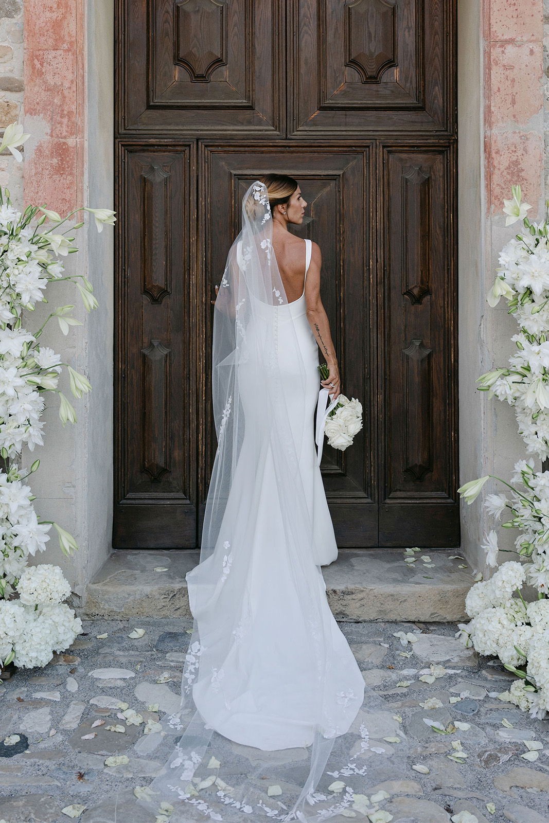 Bride standing in front of a wooden door, holding a bouquet.