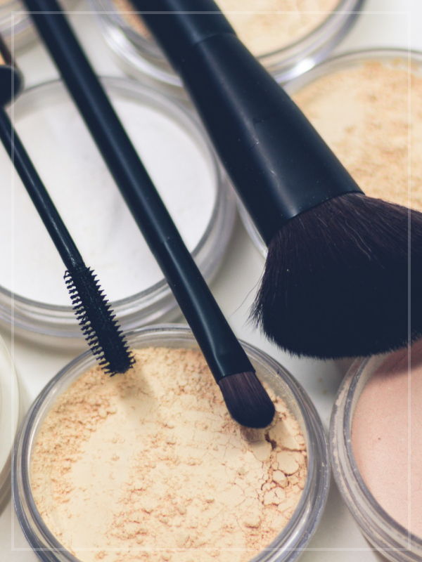 Three various sized makeup brushes over several pots of makeup