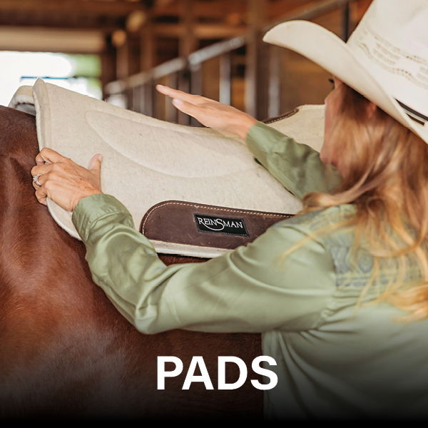 A person placing a saddle pad on a horse in a barn.