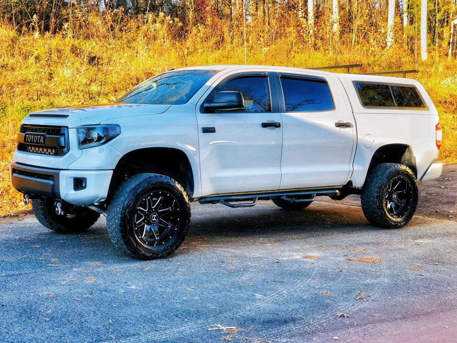 Front three-quarter Anthony's white 2014 Toyota Tundra lifted black grille TOYOTA lettering LED light bar camper shell roof rack golden hour Outlaw 127H featured customer install gallery photo 1