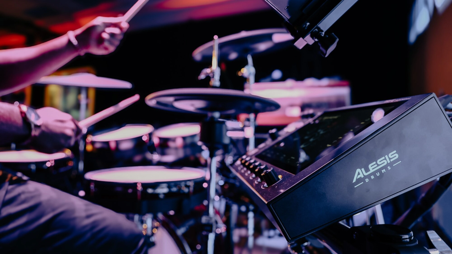 Close-up of a drummer playing Alesis electronic drums with colourful stage lighting.