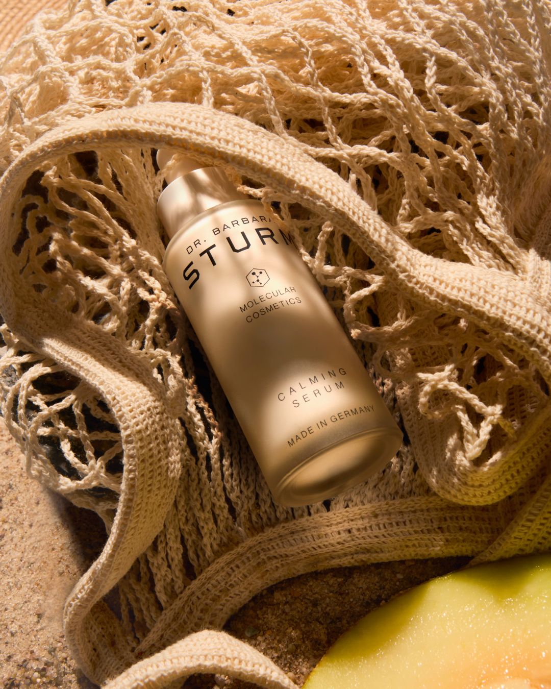 A bottle of skincare product nestled in a beige net bag.