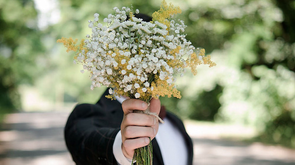 groom holding up flowers in front of his face
