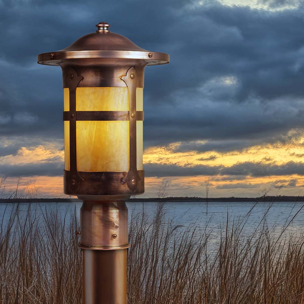 A Spanish Revival style post light, with a raw copper finish, in front of a lake at sunset.
