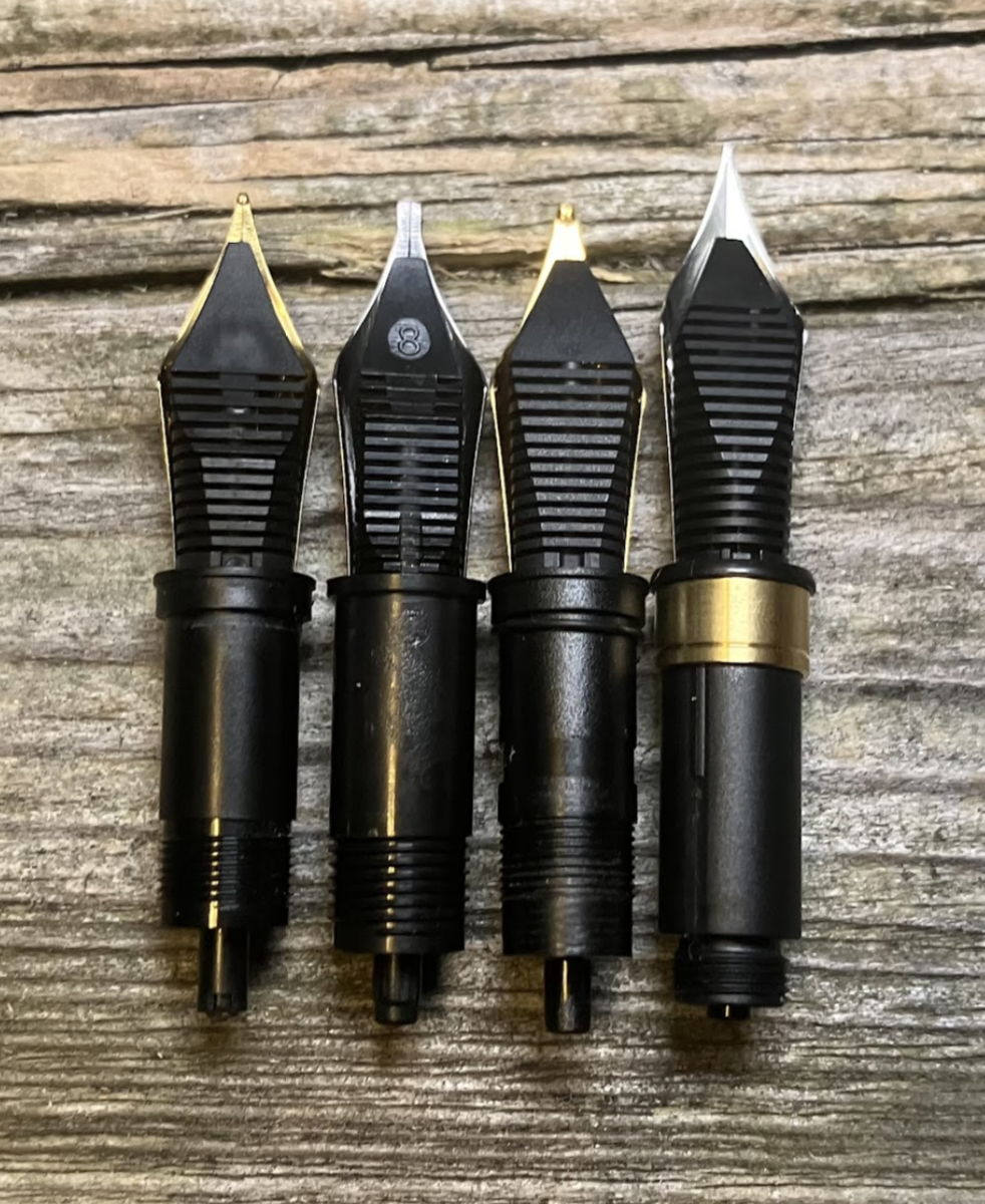 Four types of replacement fountain pen nibs resting on a wooden surface