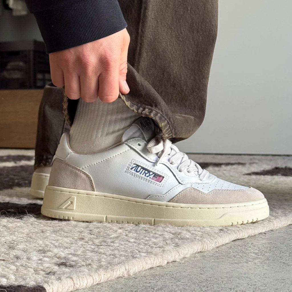 Person adjusting pants while wearing stylish sneakers on a rug.