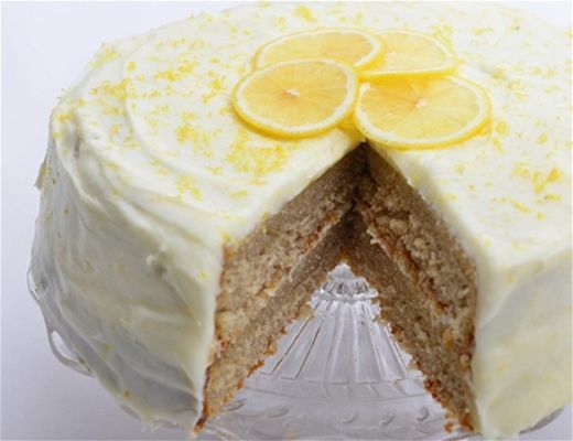 Lemon cake with frosting and lemon slices on top, partially sliced.