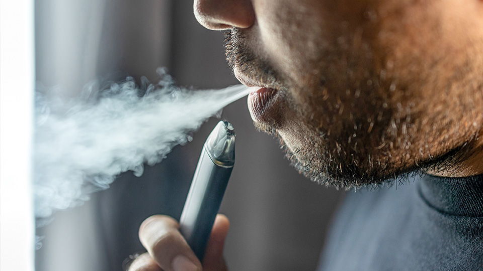 A picture of a person exhaling vapour while using an electronic vaping device indoors.