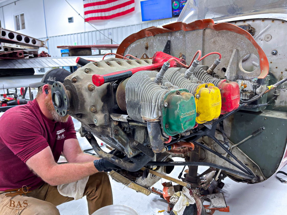 Person working on an aircraft engine in a hangar with tools and equipment.
