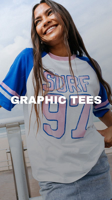 Smiling woman wearing a surf-themed graphic tee by the beach.