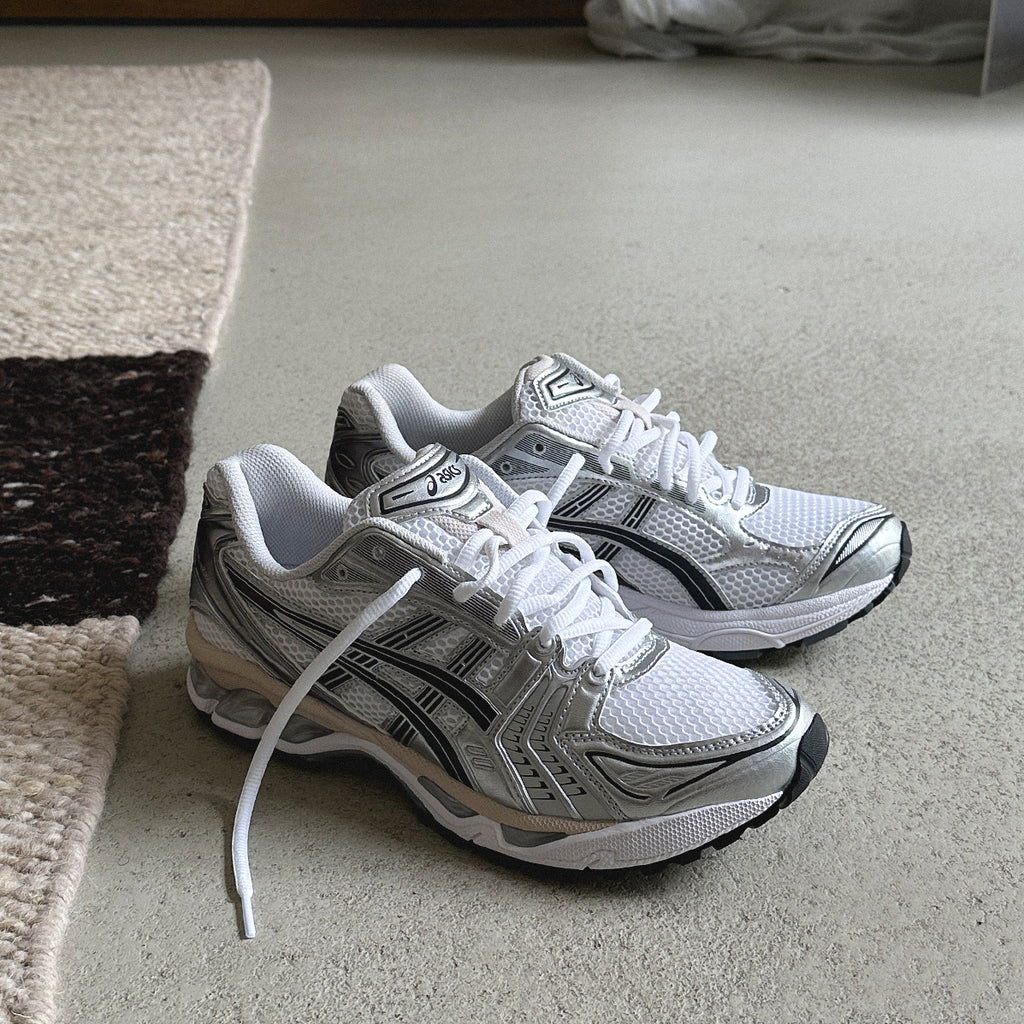 A pair of white and silver athletic shoes on a floor.