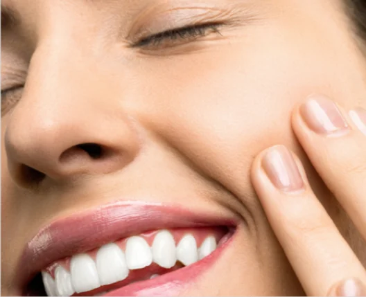 Smiling woman touching her cheek, showcasing healthy skin and bright teeth.