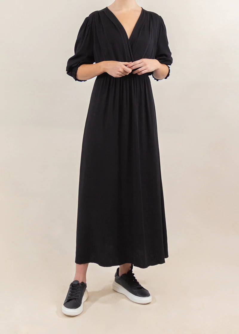 Model wearing a black v-neck dress with black trainers