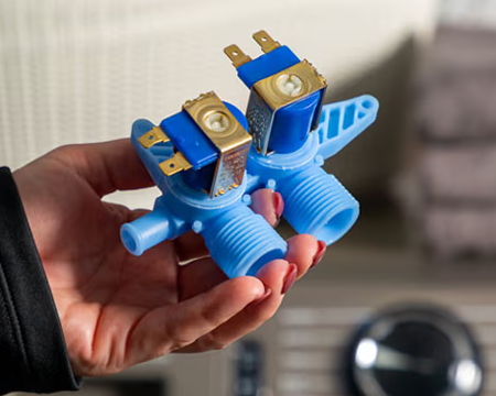 A person holding a blue dual solenoid valve assembly.