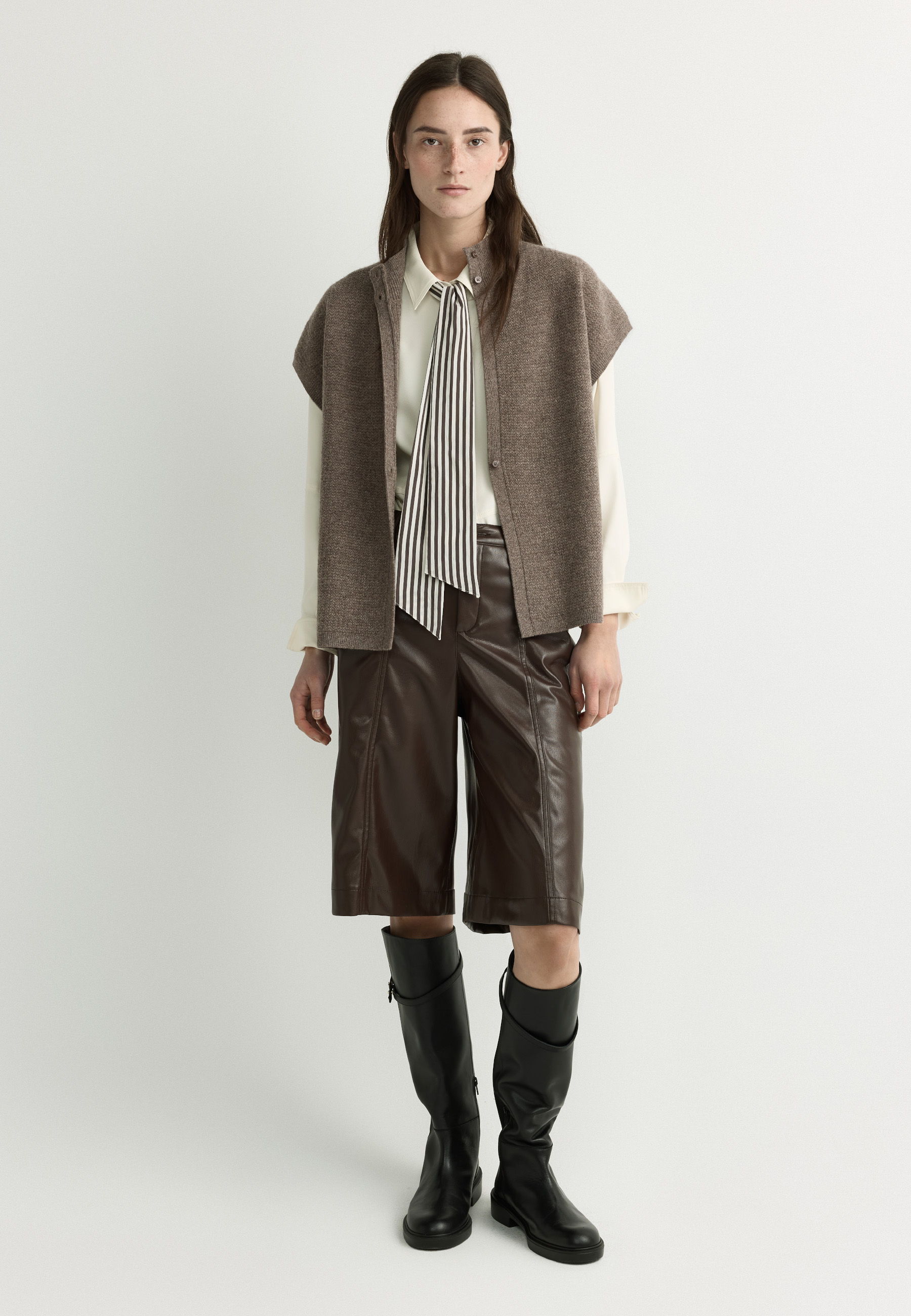 Model wearing a brown vest, white shirt, brown shorts, and black boots.
