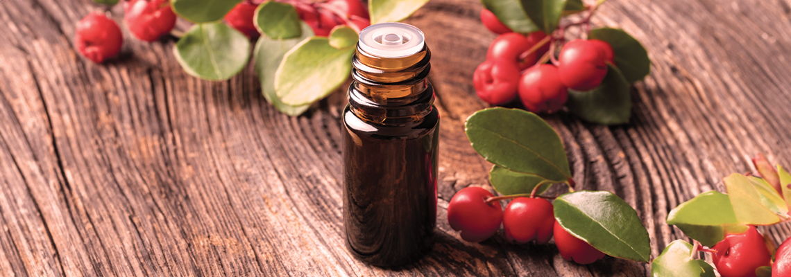 Brown glass bottle with leaves and berries on a wooden surface.