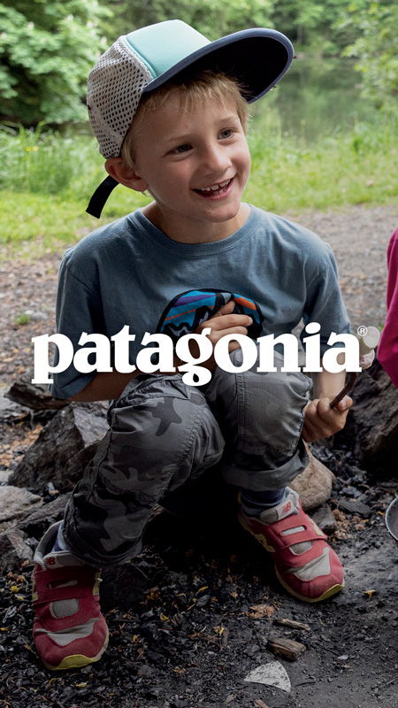 Smiling child sitting on rocks, wearing a Patagonia t-shirt and cap.