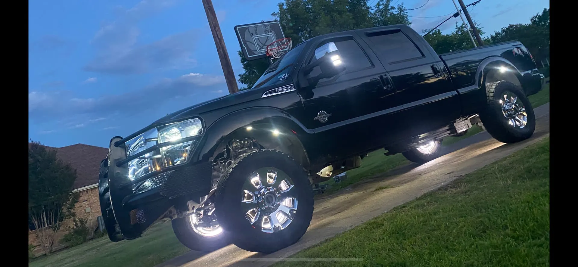 Malachi's lifted black 2012 Ford F250 with LED rock lights and chrome wheels photographed at dusk