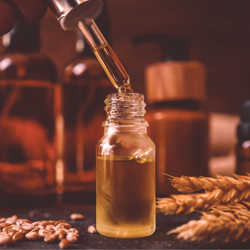 A dropper pouring oil into a small glass bottle with wheat grains.