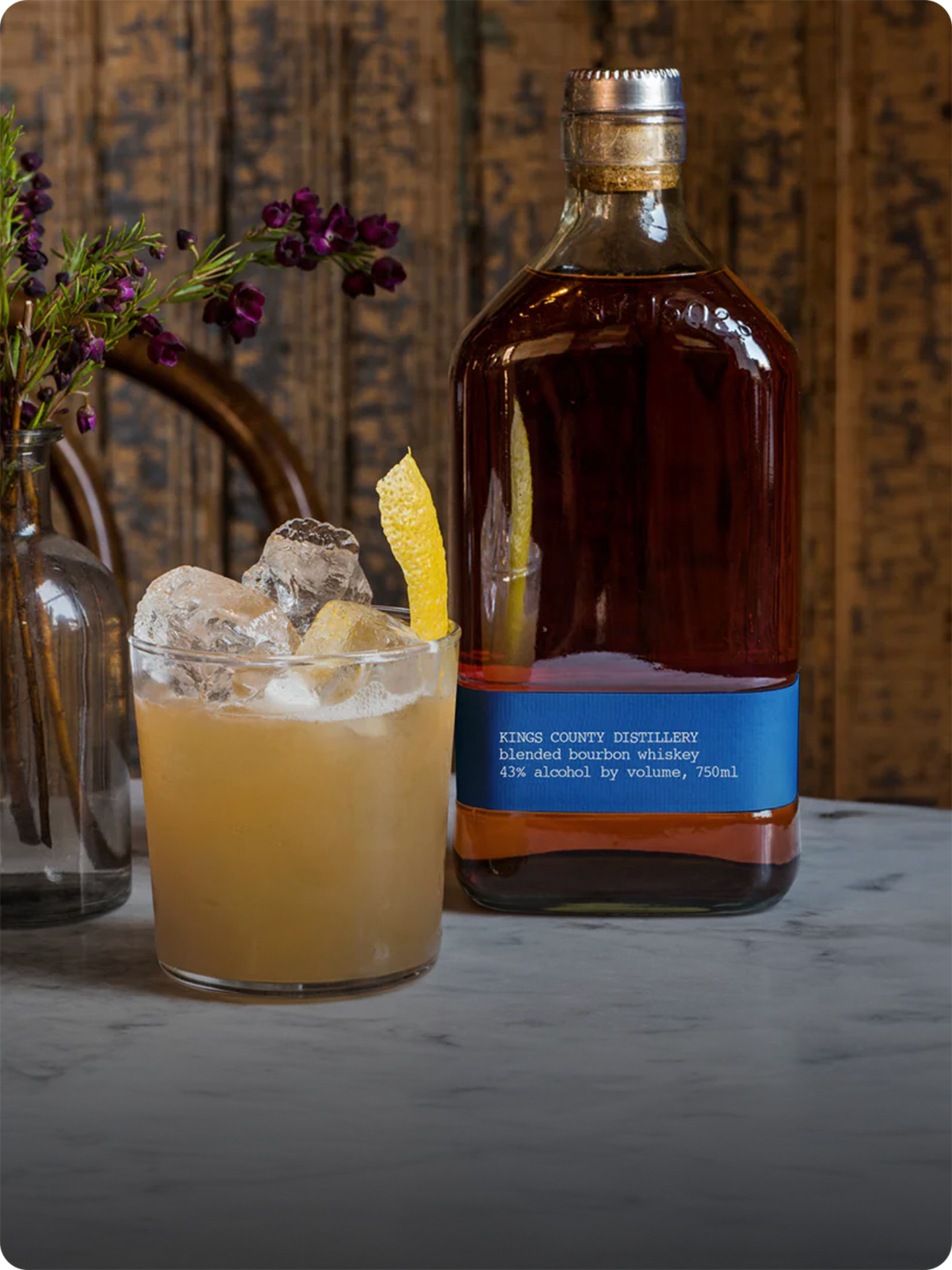 Cocktail with ice and lemon beside a whiskey bottle on a table.