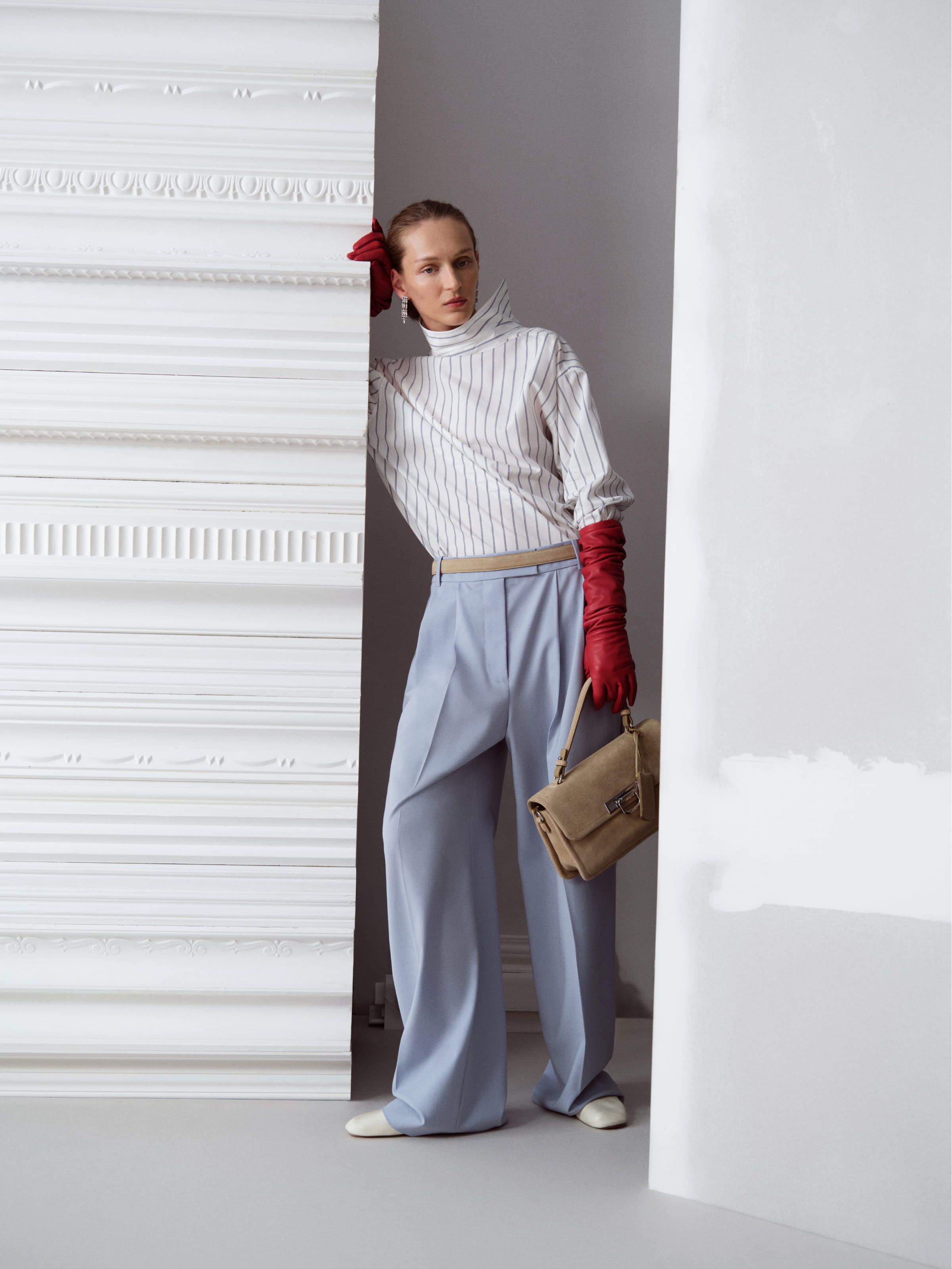 A person in stylish attire poses between two white panels.